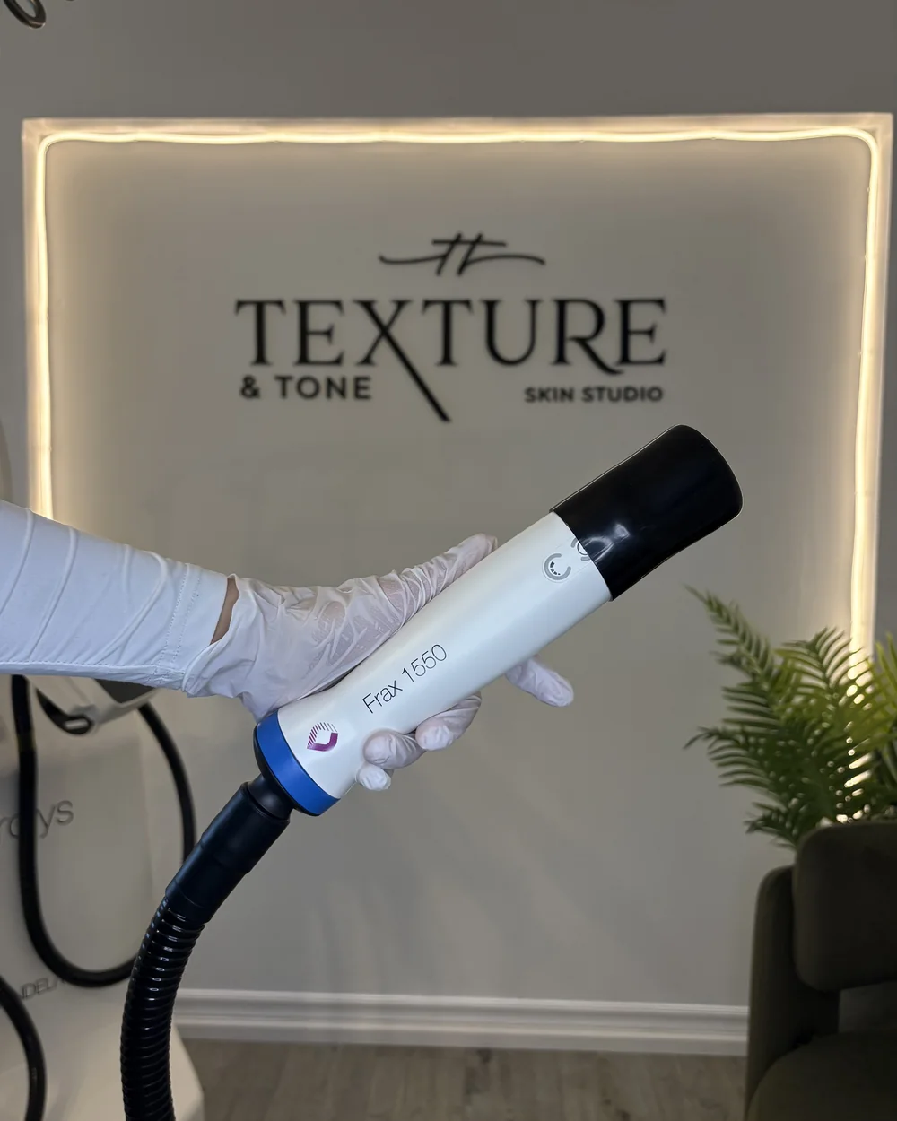 The Frax 1550 handpiece in front of the Texture & Tone logo wall